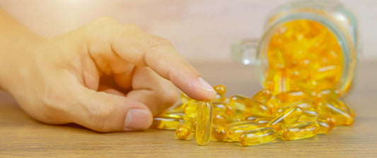 Een hand die grijpt naar omega 3 visolie capsules op tafel