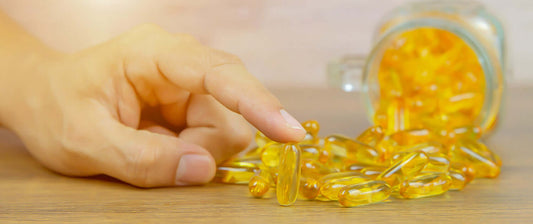 Een hand die grijpt naar omega 3 visolie capsules op tafel