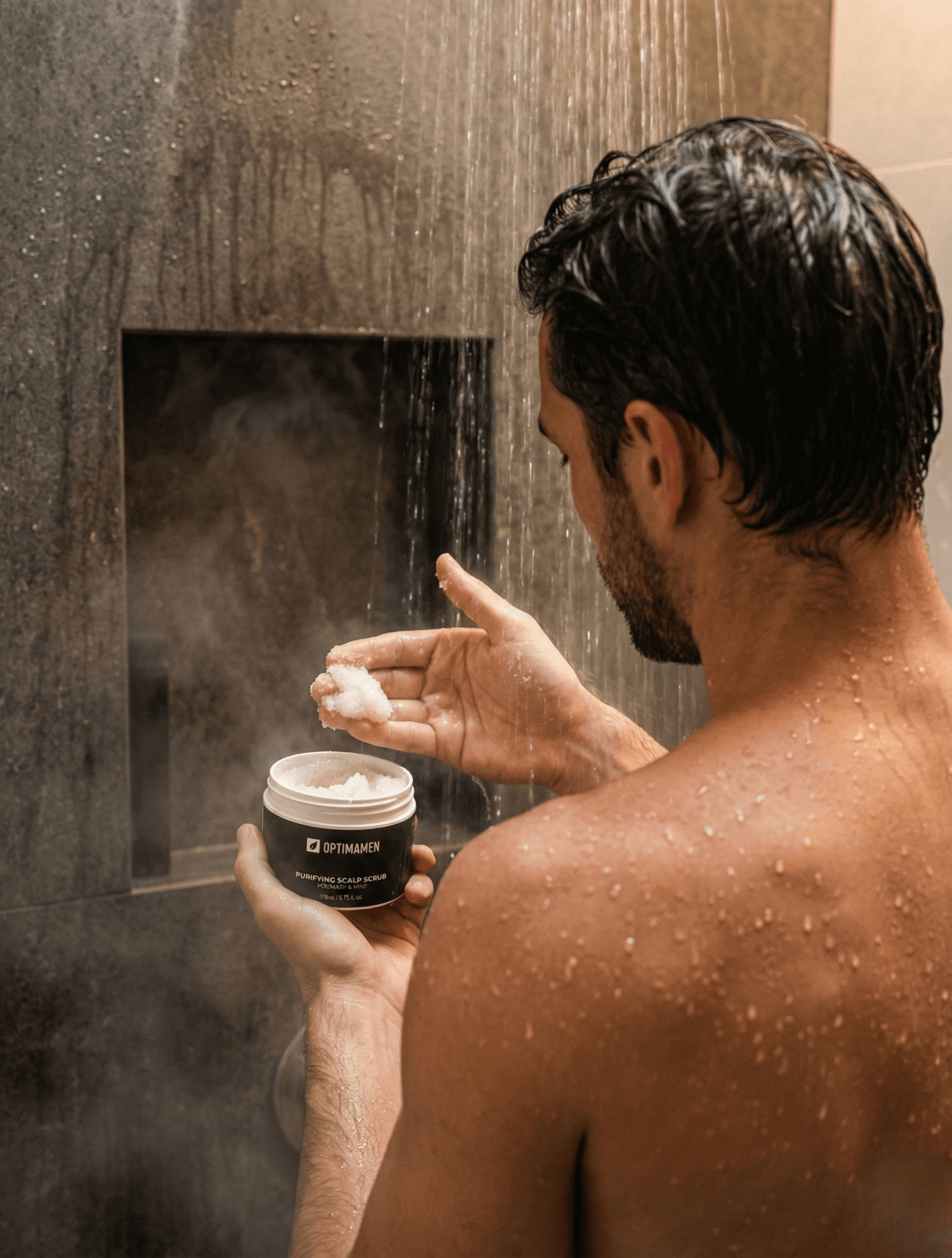 Exfoliëren van de hoofdhuid: man gebruikt OPTIMAMEN scalp scrub met rozemarijn om de doorbloeding en gezonde haargroei te stimuleren.