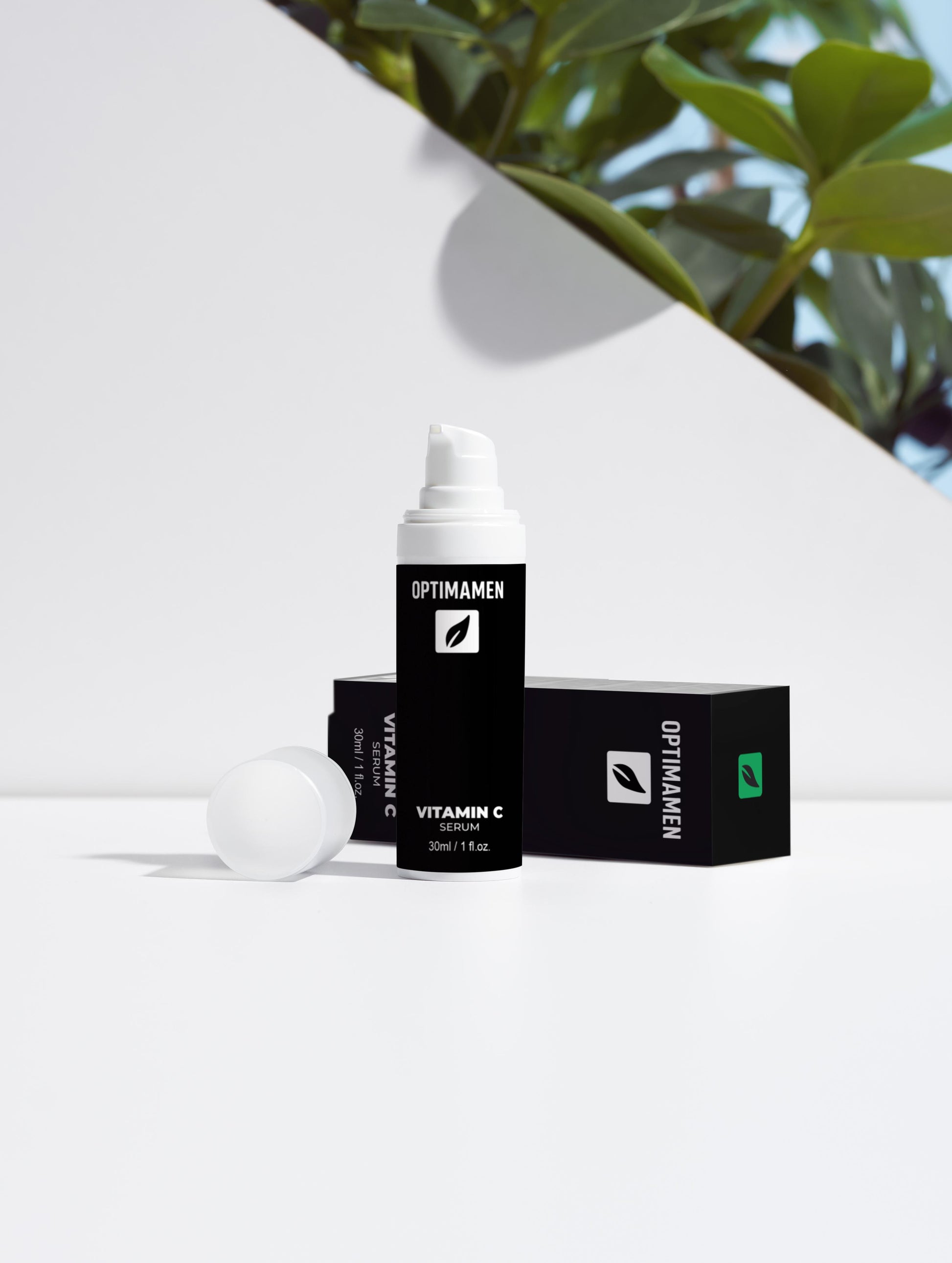 Vitamine C serum voor mannen in een zwarte verpakking op een witte achtergrond met groene bladeren als decoratie