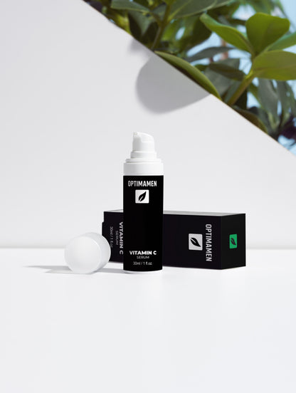 Vitamine C serum voor mannen in een zwarte verpakking op een witte achtergrond met groene bladeren als decoratie